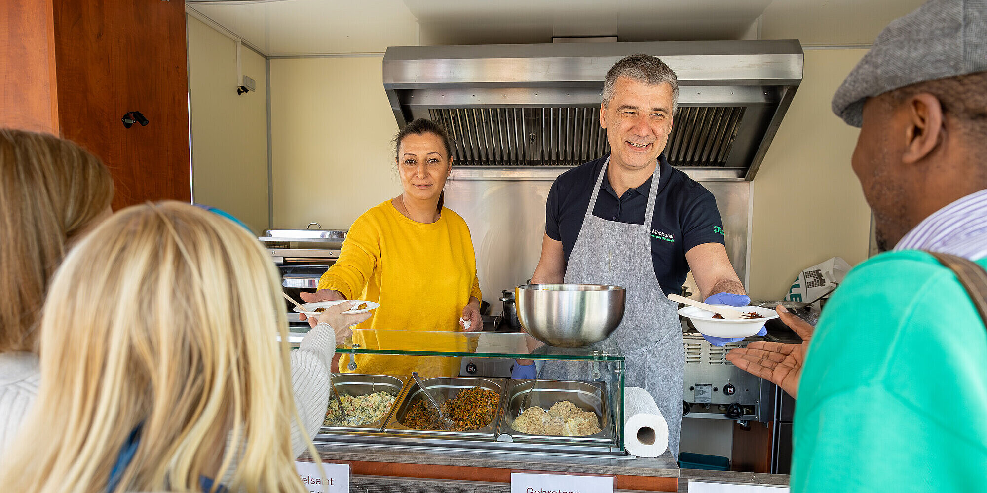 Die Mitarbeiter des Foodtrucks Incluisine geben Essen an Gäste aus.