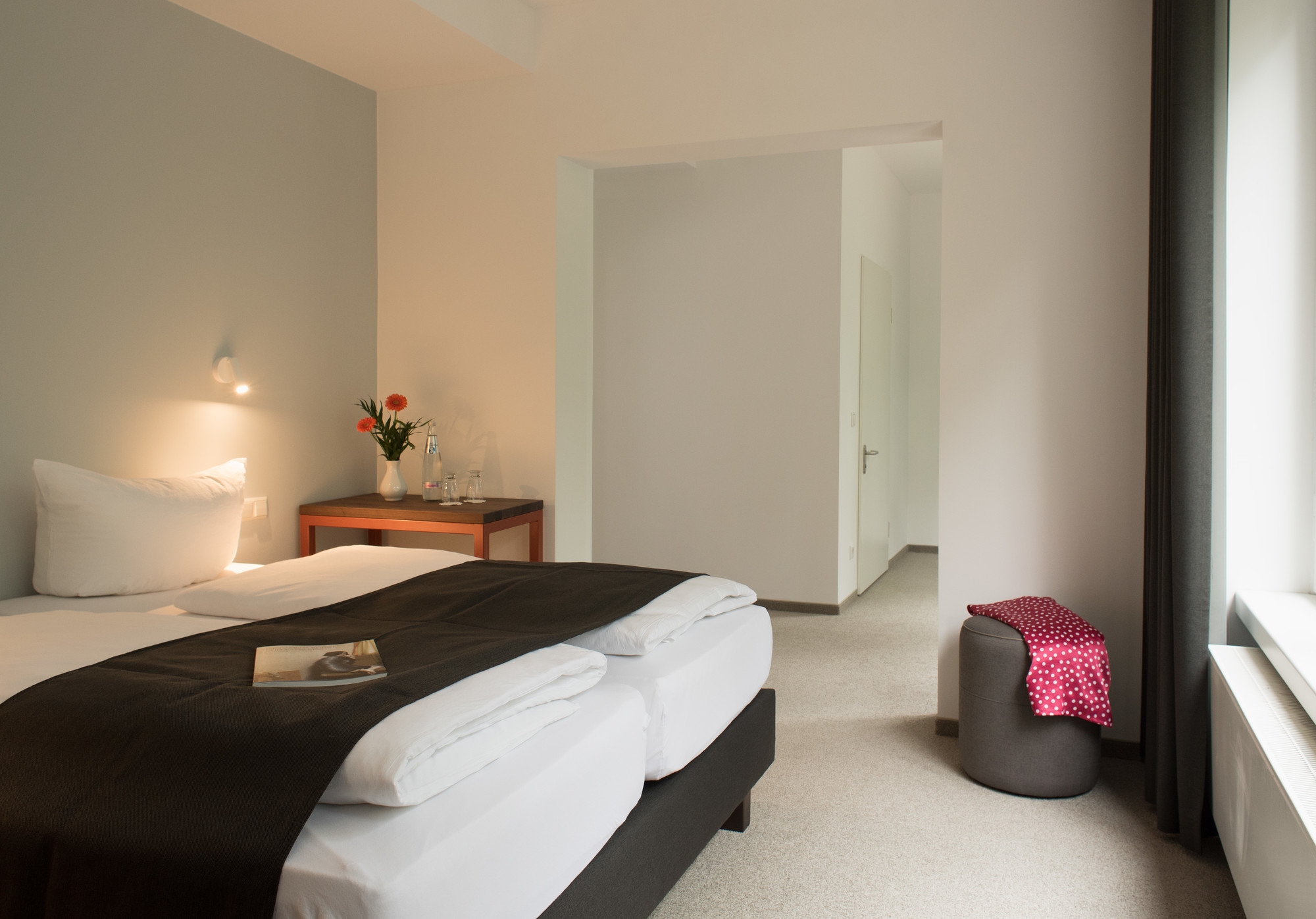 Hotelzimmer mit Doppelbett und großem Fenster. Neben dem Bett stehen Nachttische mit Lampen.