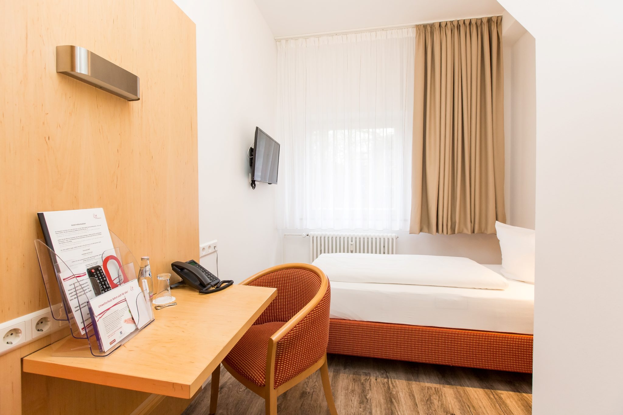Helles Einzelzimmer mit Bett, Schreibtisch und Sessel.